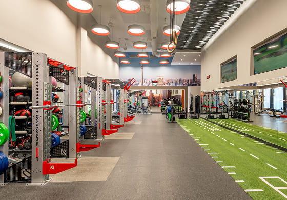 Wide view of the Toronto Athletic Club Strength Lab, featuring functional training equipment, free weights, and a turf sprint lane, with a panoramic Toronto skyline mural in the background